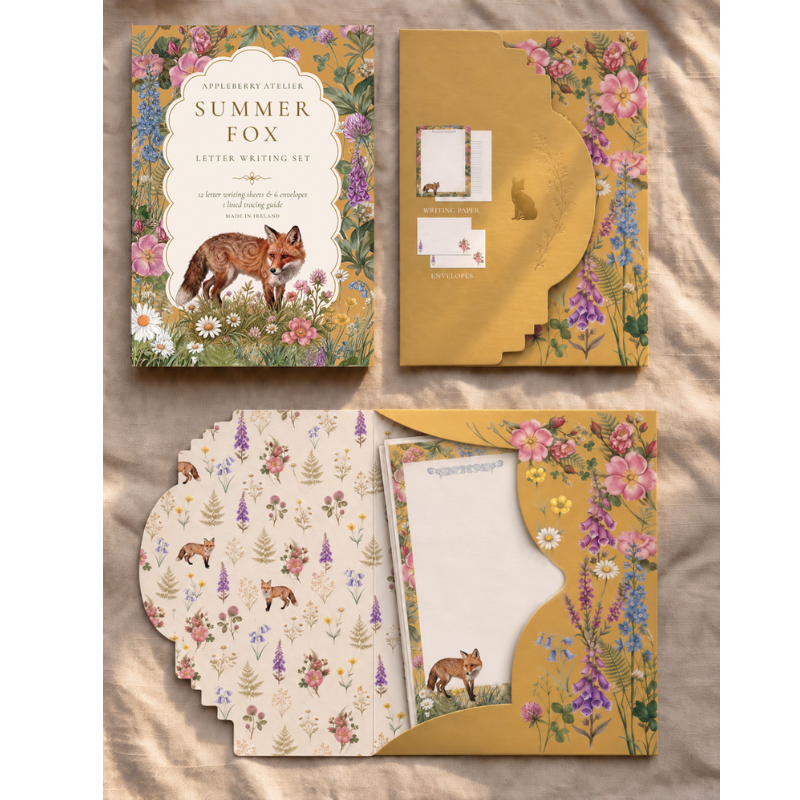 A flat-lay presentation of the Appleby's Summer Fox Letter Writing Set, showing the illustrated book cover, a gold envelope, patterned stationery sheets, and a letterhead card on a textured beige fabric background.