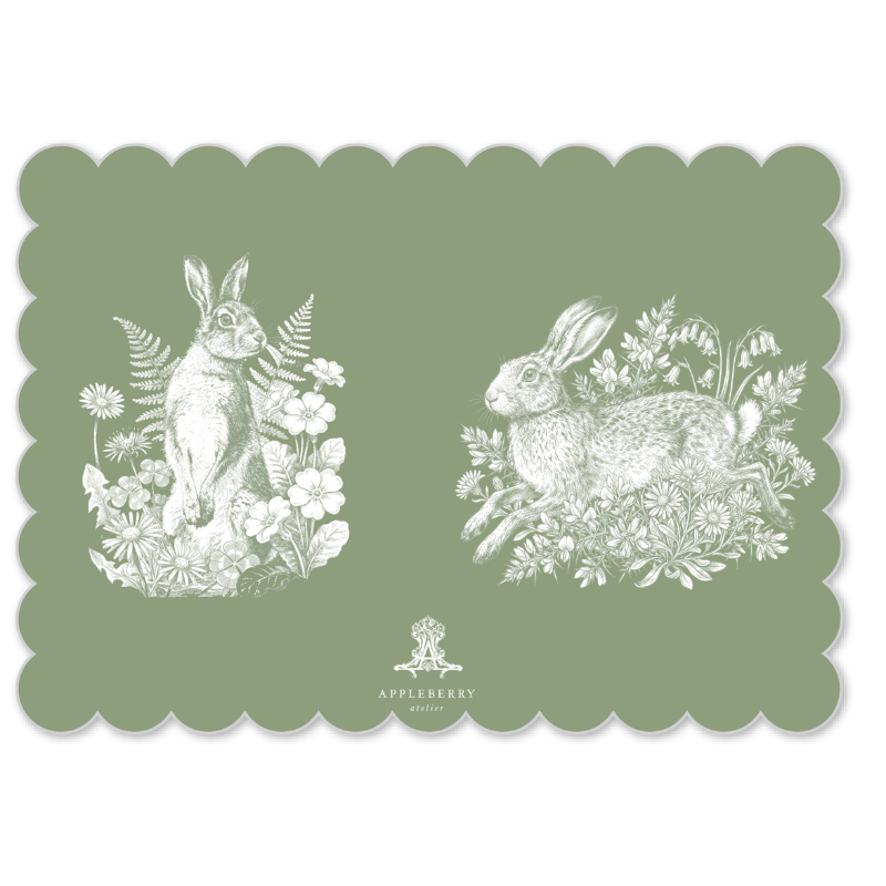 A square green placemat with scalloped edges featuring white line drawings of two rabbits in a floral setting, with the Appleberry Gardens logo at the bottom center.