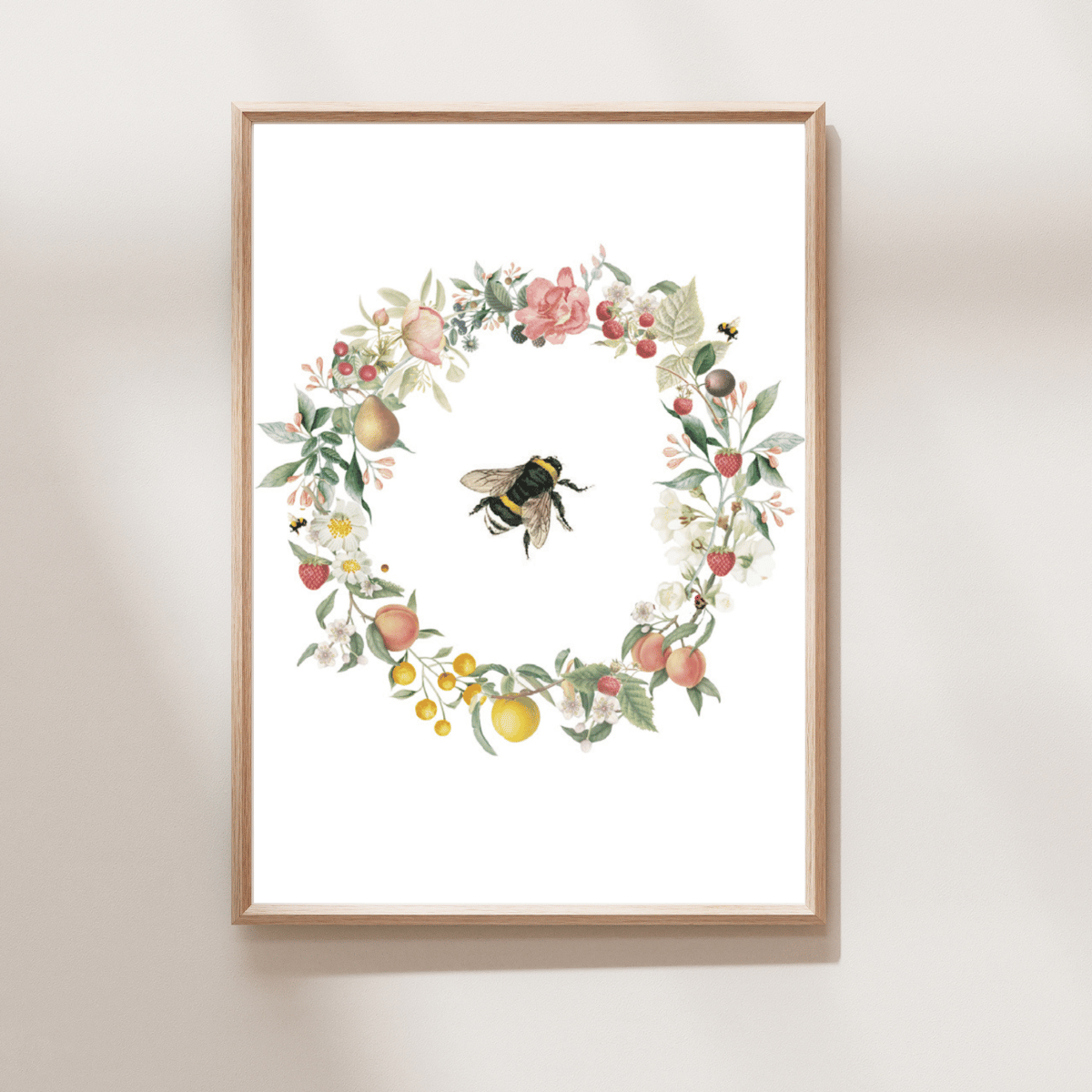Framed botanical art print featuring a circular wreath of pink flowers, green leaves, and fruit with a bumblebee at the center, displayed on a light beige wall.