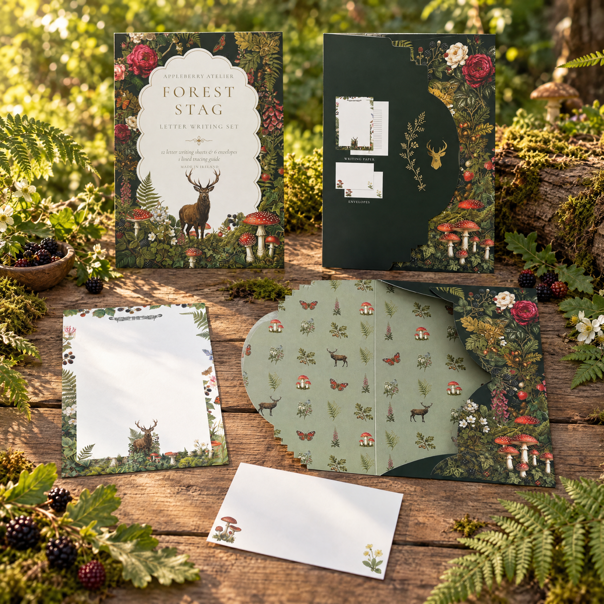 A forest-themed stationery set arranged on a rustic wooden surface with greenery and berries. The set includes a main letterhead card, a dark storage envelope, letter paper, and a coordinating envelope, all decorated with woodland illustrations like deer, mushrooms, and foliage.