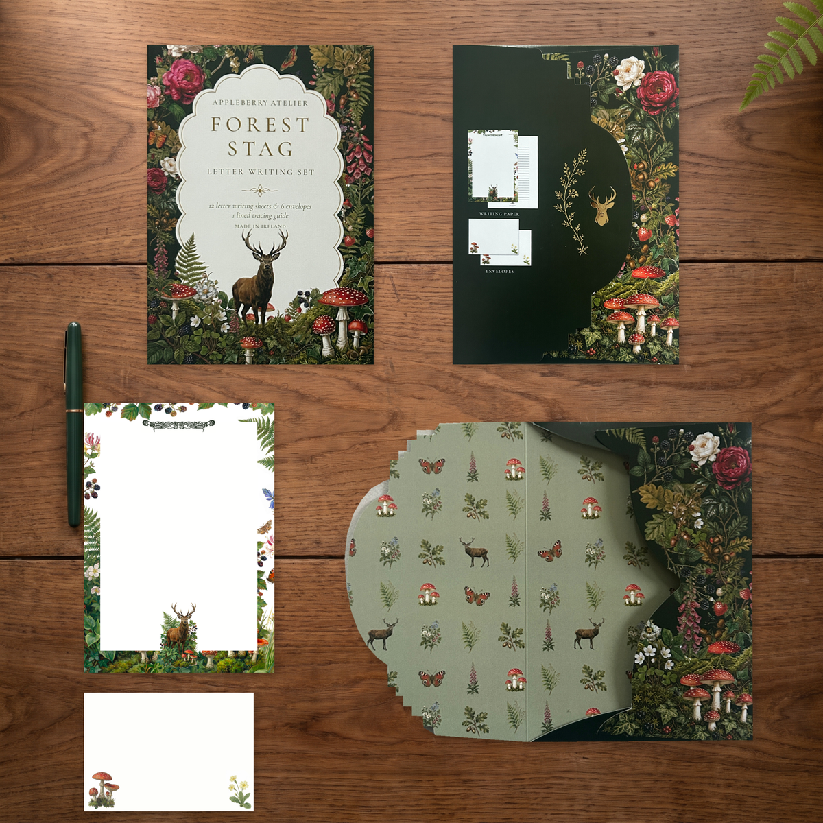 A forest-themed letter writing set arranged on a wooden tabletop, including storage envelope, writing paper and envelopes. The stationery features woodland illustrations such as a stag, mushrooms, flowers, and trees, with one card reading 'Forest Stag Letter Writing Set.