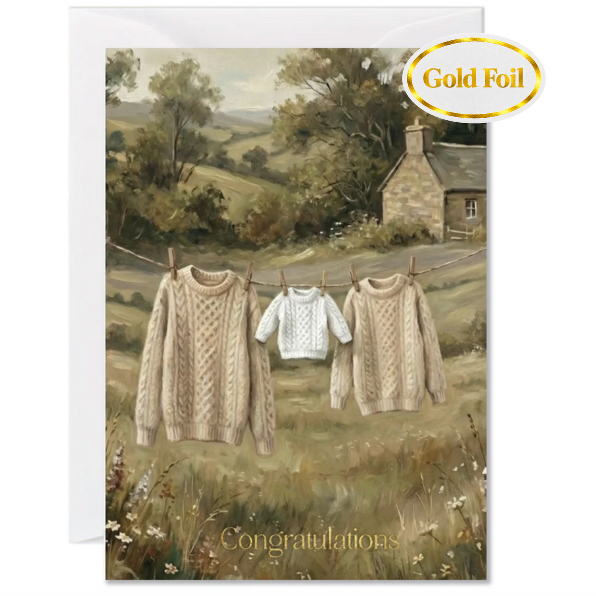 A greeting card featuring a pastoral countryside scene with three cable-knit sweaters in large, medium and 'baby size ' hanging on a clothesline in front of a stone cottage. 'Congratulations' is shown in gold foil at the bottom of the card. The card includes a white envelope behind it and a gold foil 'Gold Foil' badge in the top right corner.