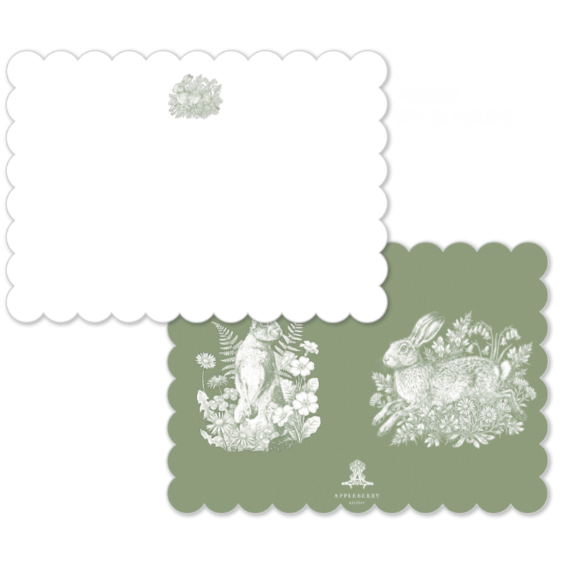 Two scalloped-edge paper napkins or cards on a white background. One is plain white with a small pale green floral motif near the top, and the other is sage green with white illustrated animal and floral artwork plus a small logo at the bottom.