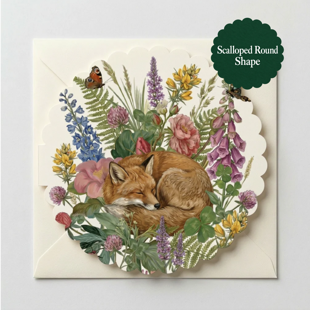 A scalloped round greeting card featuring an illustration of a sleeping fox surrounded by colorful wildflowers, shown with its matching cream envelope on a light gray background. A dark green circular badge in the top right reads 'Scalloped Round Shape'.