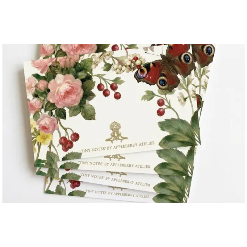 A stack of botanical-themed stationery cards or note pads from Appleberry Atelier, featuring pink roses, green leaves, red berries, and a peacock butterfly on a white background.