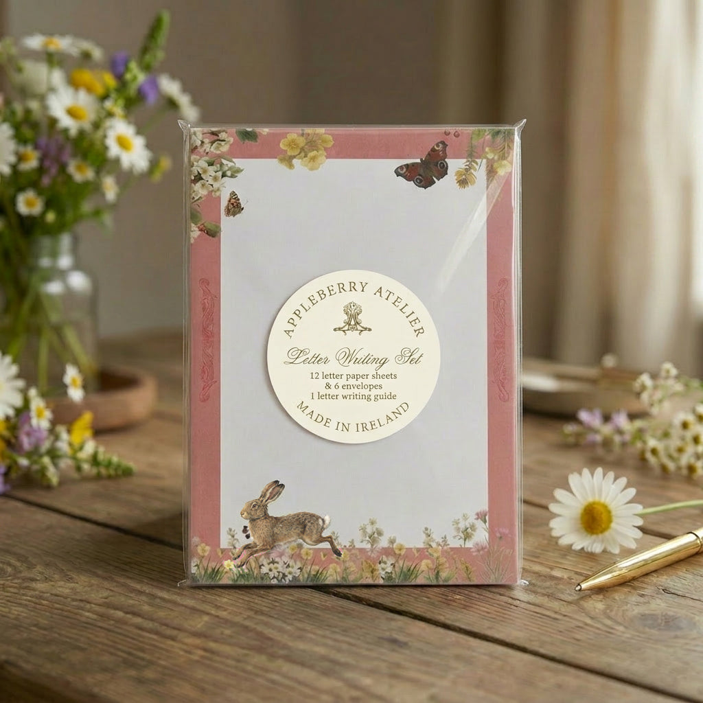 Packaged letter writing set with floral design on a wooden table with flowers and a pen.
