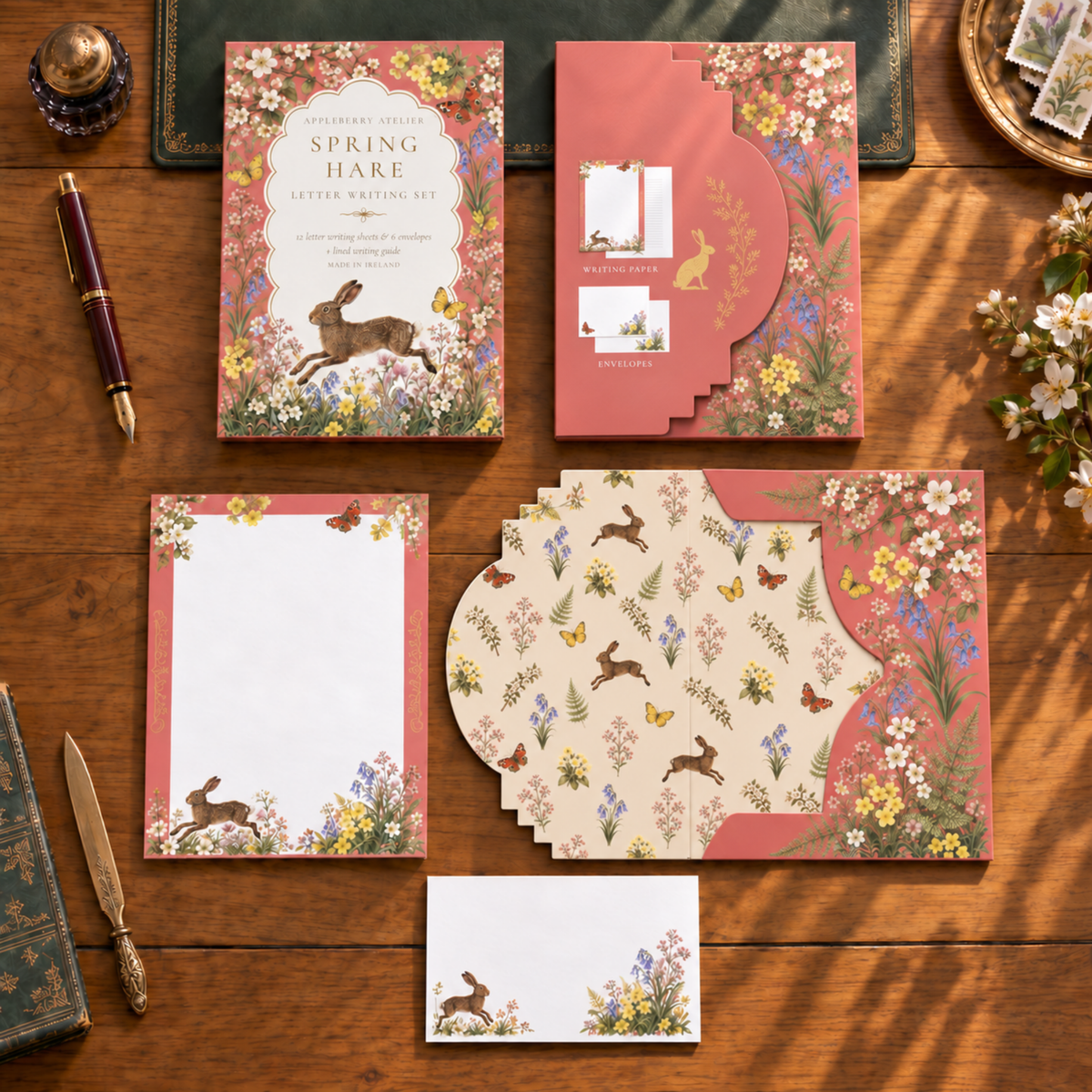 A coordinated stationery set laid out on a wooden table, featuring floral storage envelope, a letter paper, and matching envelope.. The set includes pink and cream sections with rabbit illustrations and wildflower borders.