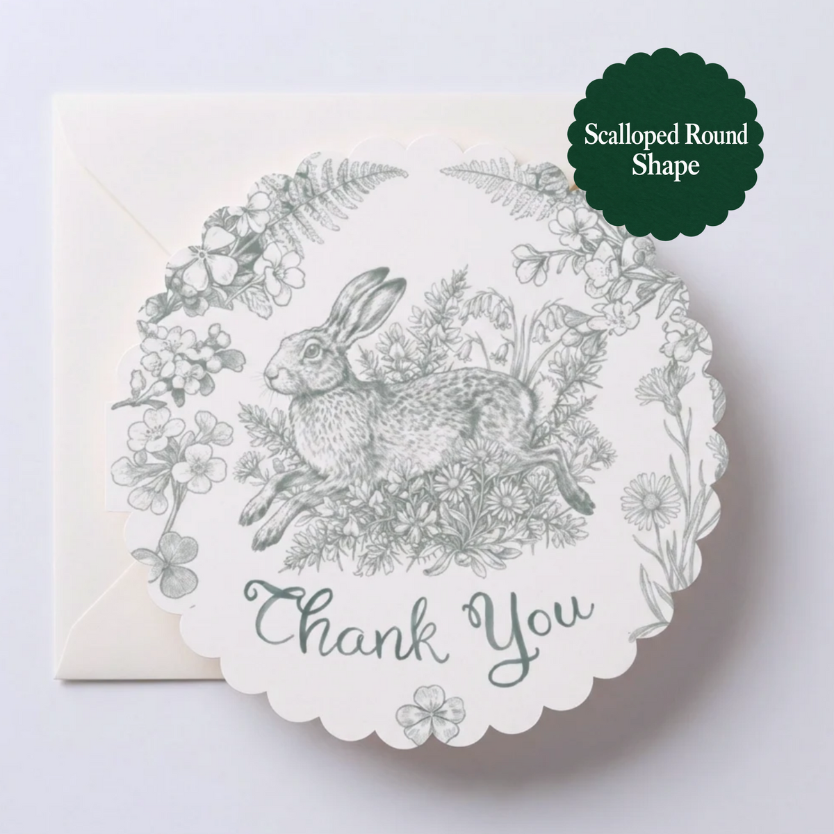 A scalloped round thank-you card with a green/grey line drawing of a rabbit among flowers and leaves, shown with a matching envelope on a light background. A dark green badge in the top right reads 'Scalloped Round Shape'.
